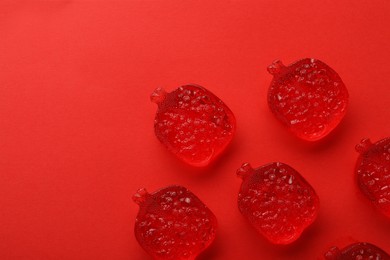 Delicious gummy pomegranate candies on red background, flat lay. Space for text