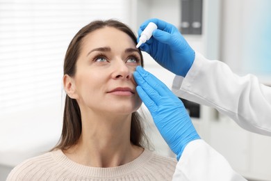 Photo of Doctor applying medical drops into woman's eye indoors