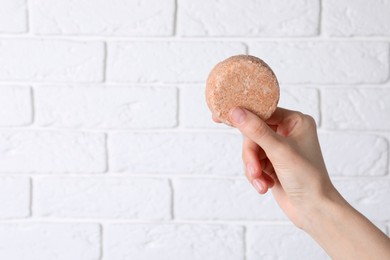 Photo of Woman holding solid shampoo bar against brick white wall, closeup. Space for text