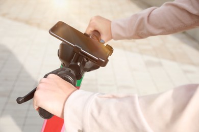 Photo of Man riding modern electric kick scooter with smartphone outdoors, closeup