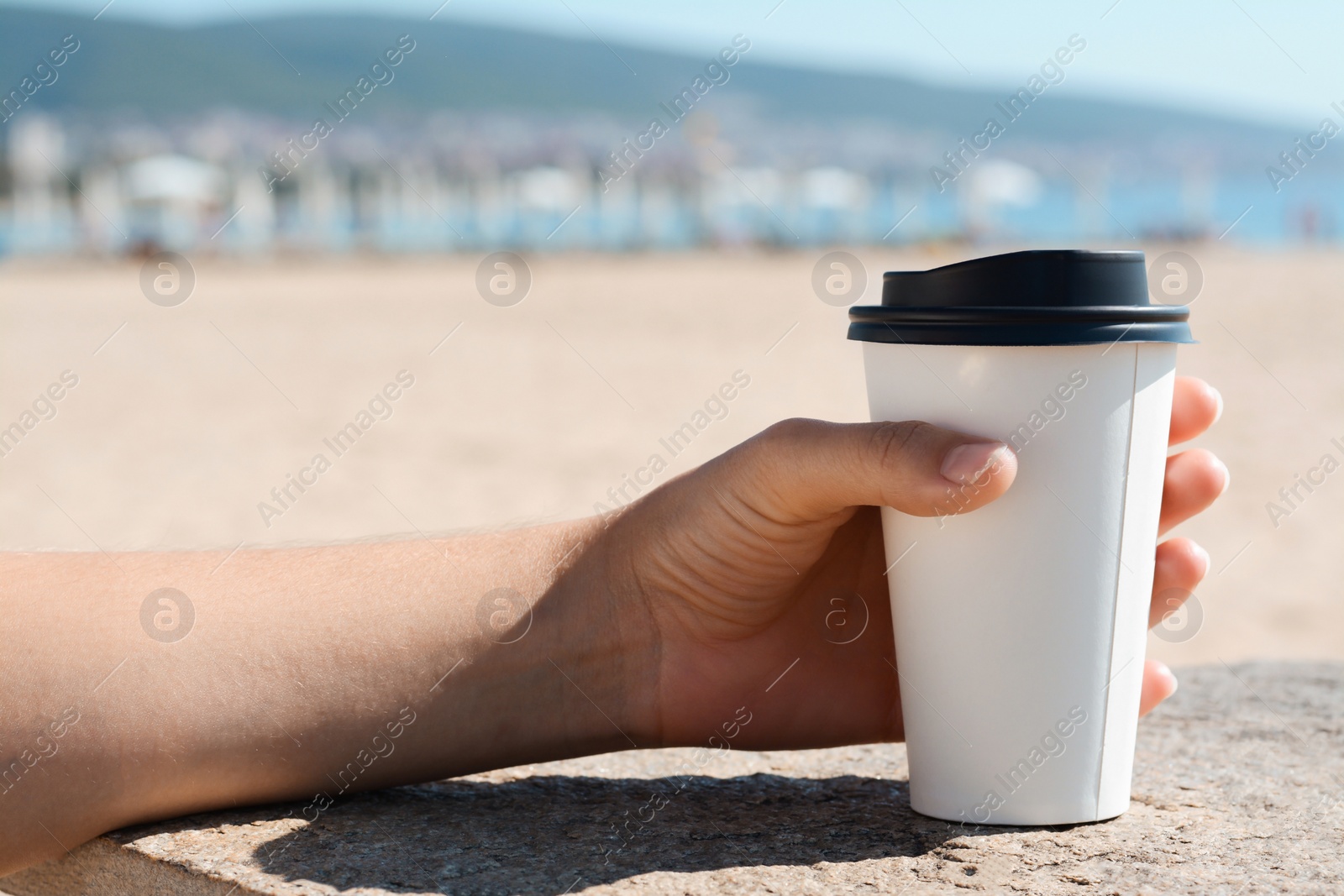 Photo of Woman with takeaway coffee cup on beach, closeup