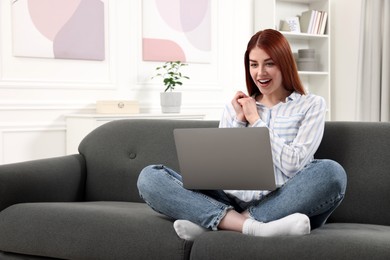 Happy woman with laptop sitting on couch in room