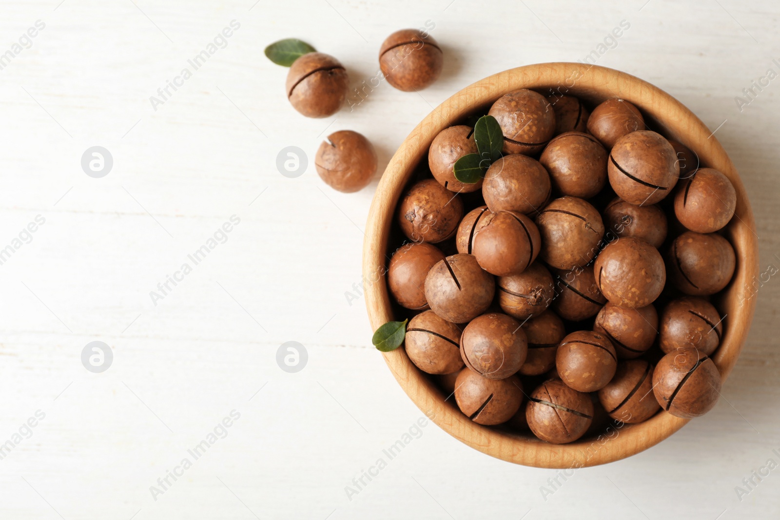 Photo of Bowl with organic Macadamia nuts and space for text on white table, top view