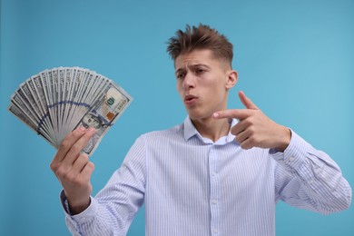 Photo of Handsome man pointing at dollar banknotes on light blue background, selective focus