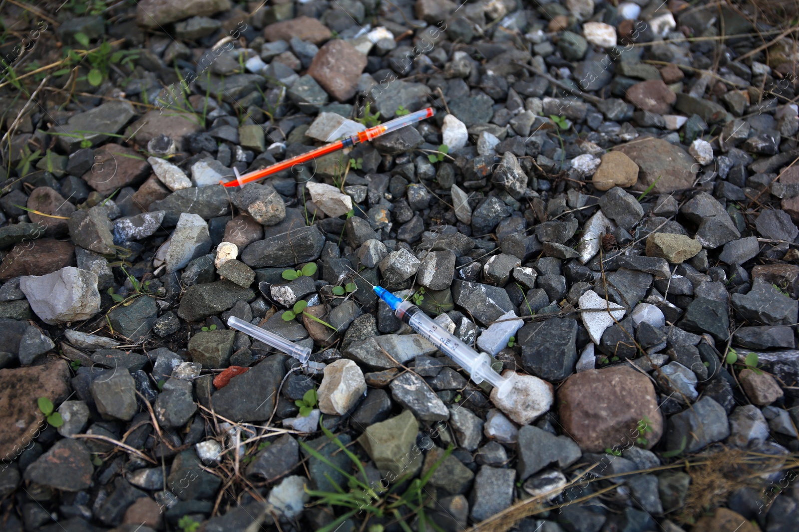 Photo of Disposable syringes with needles on heap of stones outdoors