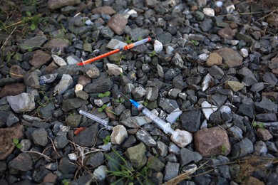 Photo of Disposable syringes with needles on heap of stones outdoors