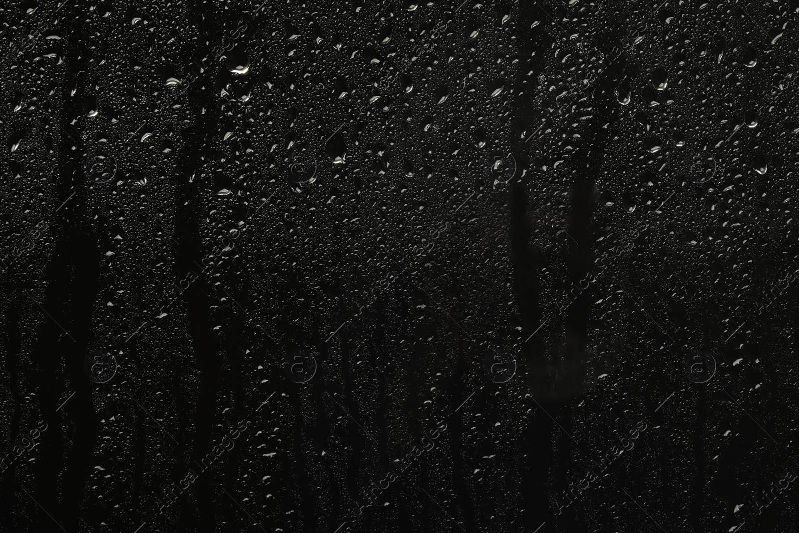 Photo of Glass with rain drops on black background