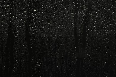 Photo of Glass with rain drops on black background