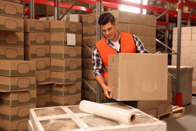 Worker with box wrapped in stretch film at warehouse