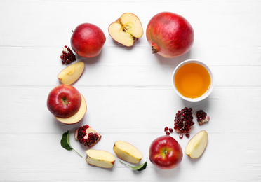 Photo of Frame of honey, apples and pomegranates on white wooden table, flat lay with space for text. Rosh Hashanah holiday