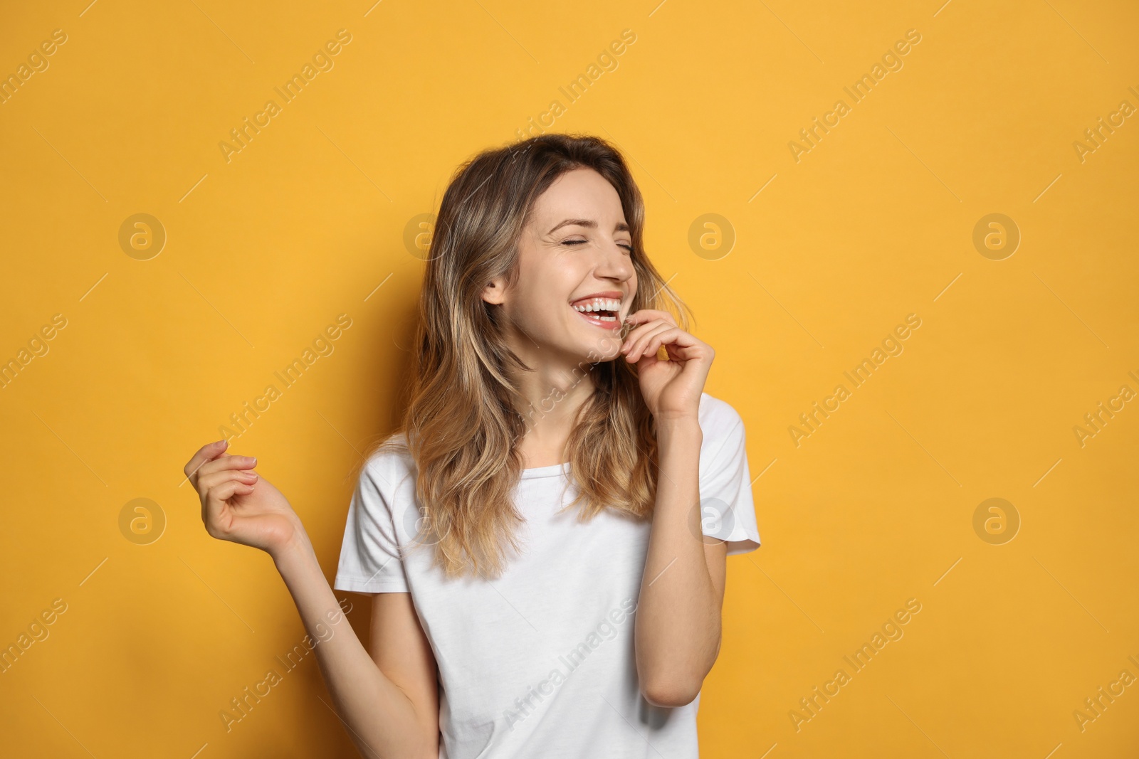 Photo of Cheerful young woman laughing on yellow background