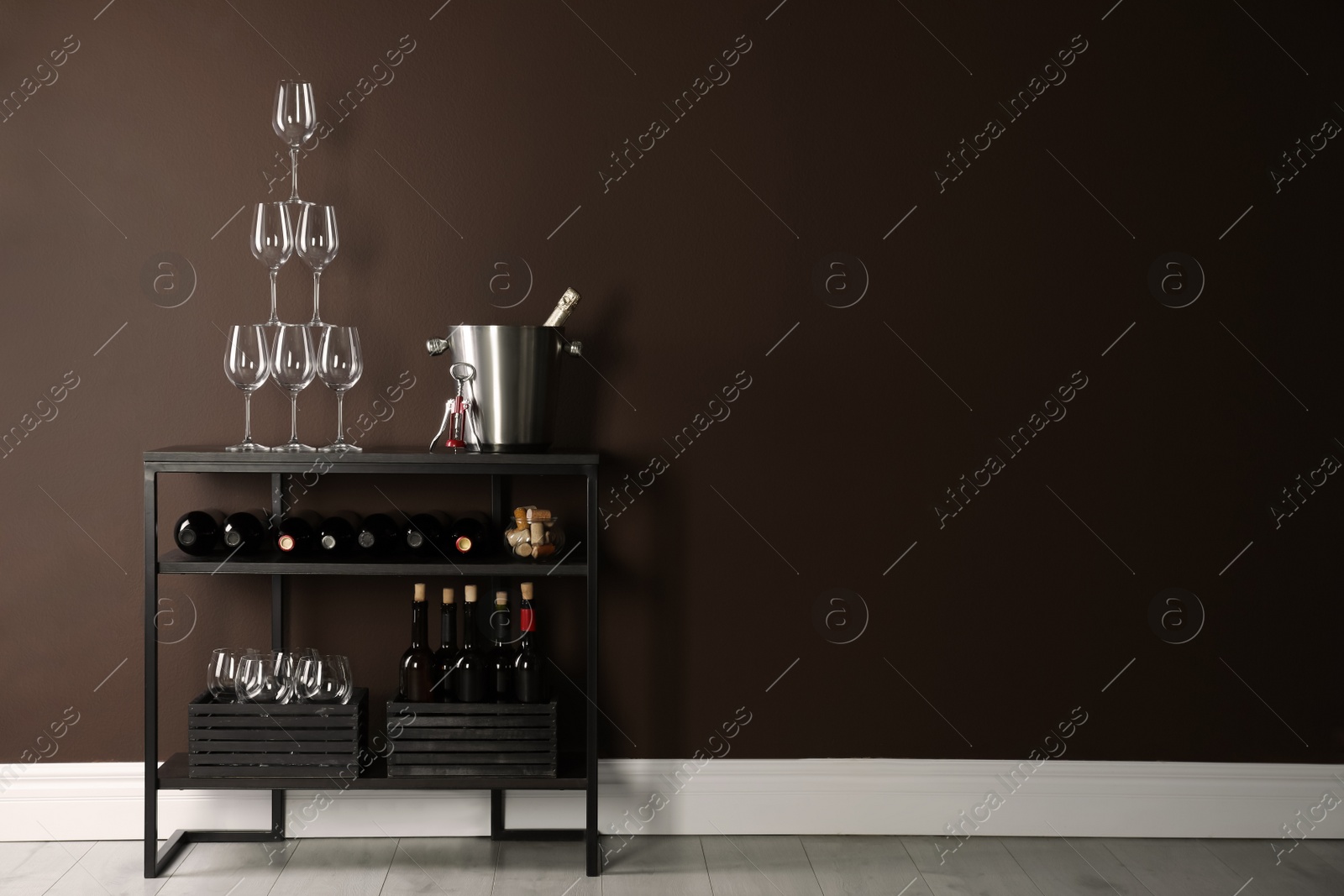 Photo of Rack with bottles of wine and glasses near brown wall, space for text