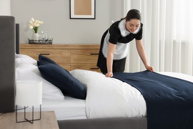 Photo of Young chambermaid making bed in hotel room