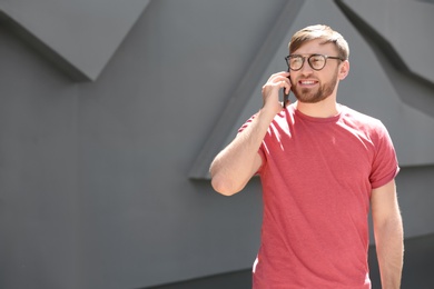 Photo of Portrait of young man talking on phone near grey wall