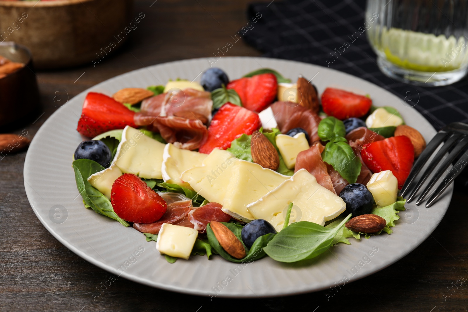 Photo of Tasty salad with brie cheese, prosciutto, almonds and berries on wooden table, closeup