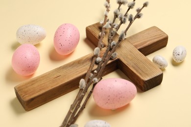 Photo of Wooden cross, painted Easter eggs and willow branches on beige background