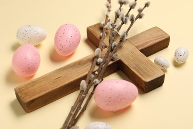 Wooden cross, painted Easter eggs and willow branches on beige background