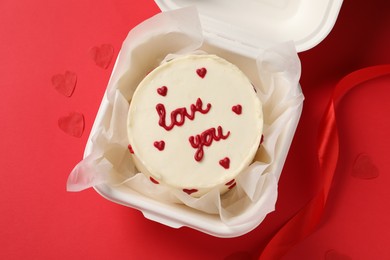 Photo of Bento cake with Love You text in takeaway box on red table, top view. St. Valentine's day surprise