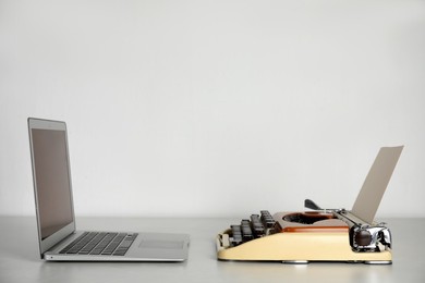 Photo of Old typewriter and laptop on table against light background, space for text. Concept of technology progress