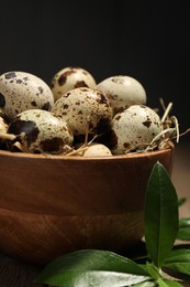 Photo of Wooden bowl with quail eggs and green leaves on table, closeup