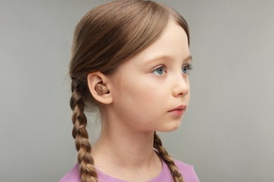 Photo of Little girl with hearing aid on grey background