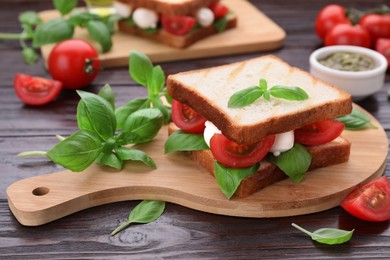 Photo of Delicious Caprese sandwich with mozzarella, tomatoes, basil and pesto sauce on wooden table