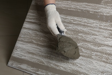 Photo of Worker holding adhesive mix on spatula above tile, closeup