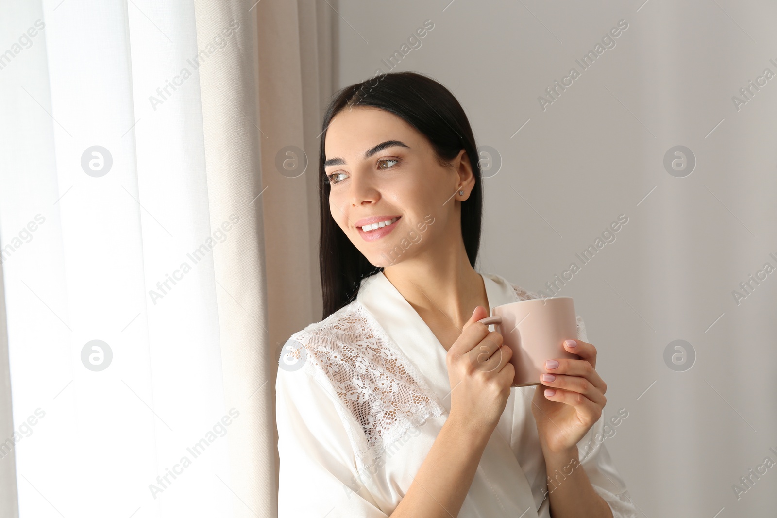 Photo of Young woman with cup of coffee near window. Lazy morning