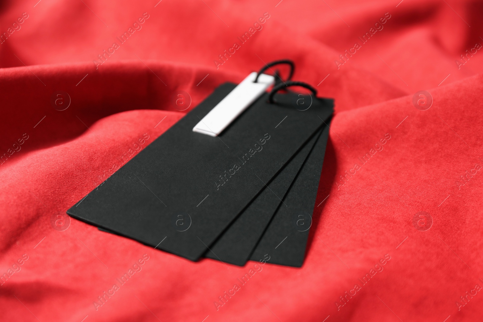 Photo of Blank black tags on red fabric, closeup. Space for text