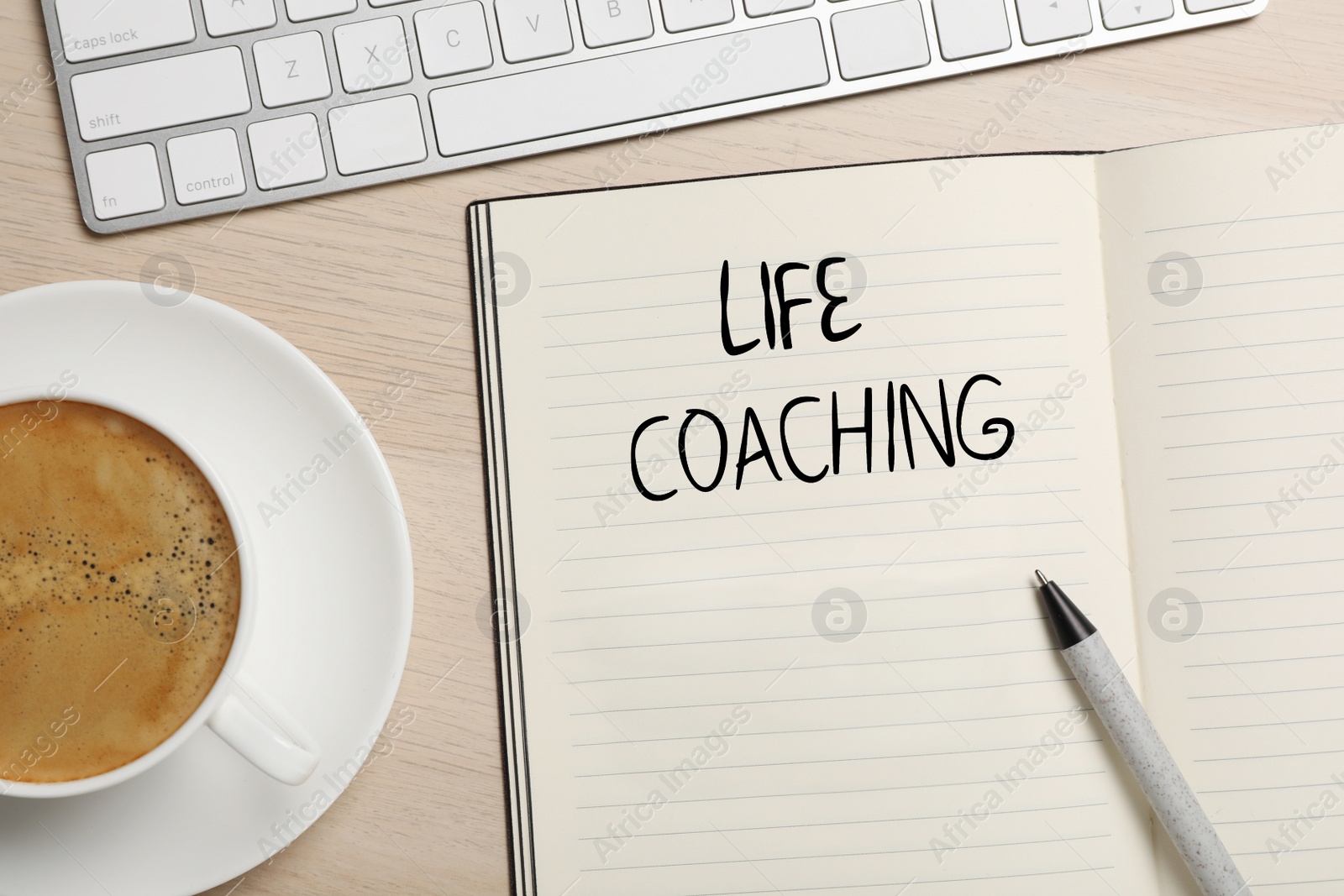 Image of Phrase Life Coach written in notebook, pen, cup of coffee and keyboard on wooden table, flat lay