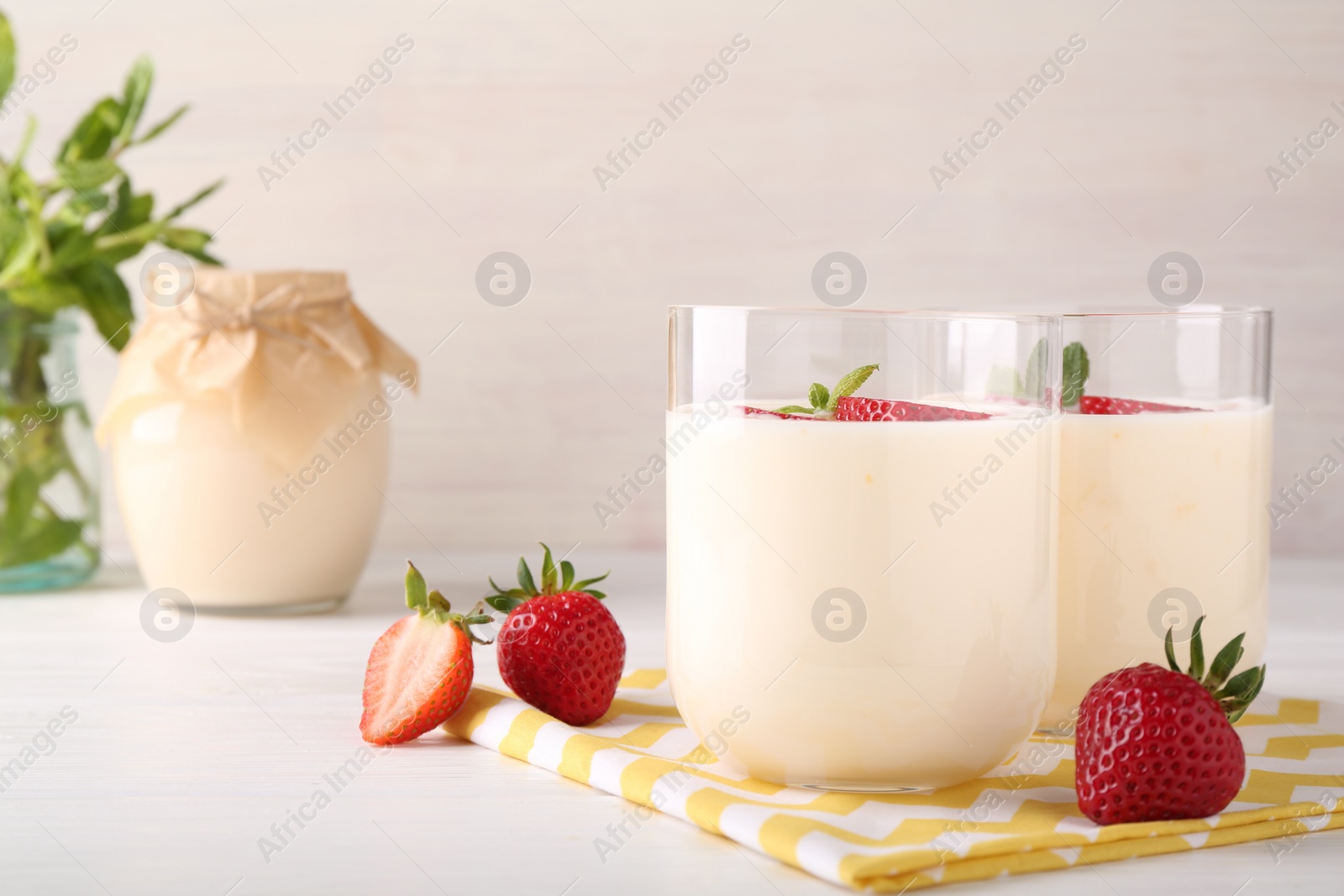 Photo of Tasty yogurt and strawberries in glasses on white wooden table, closeup. Space for text