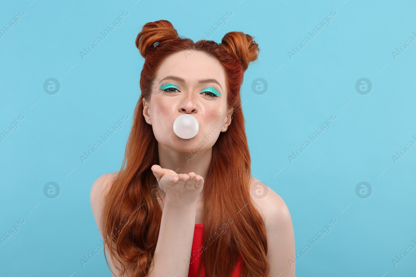 Photo of Portrait of beautiful woman with bright makeup blowing bubble gum on light blue background