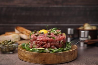 Photo of Tasty beef steak tartare served with yolk, capers and microgreens on brown table
