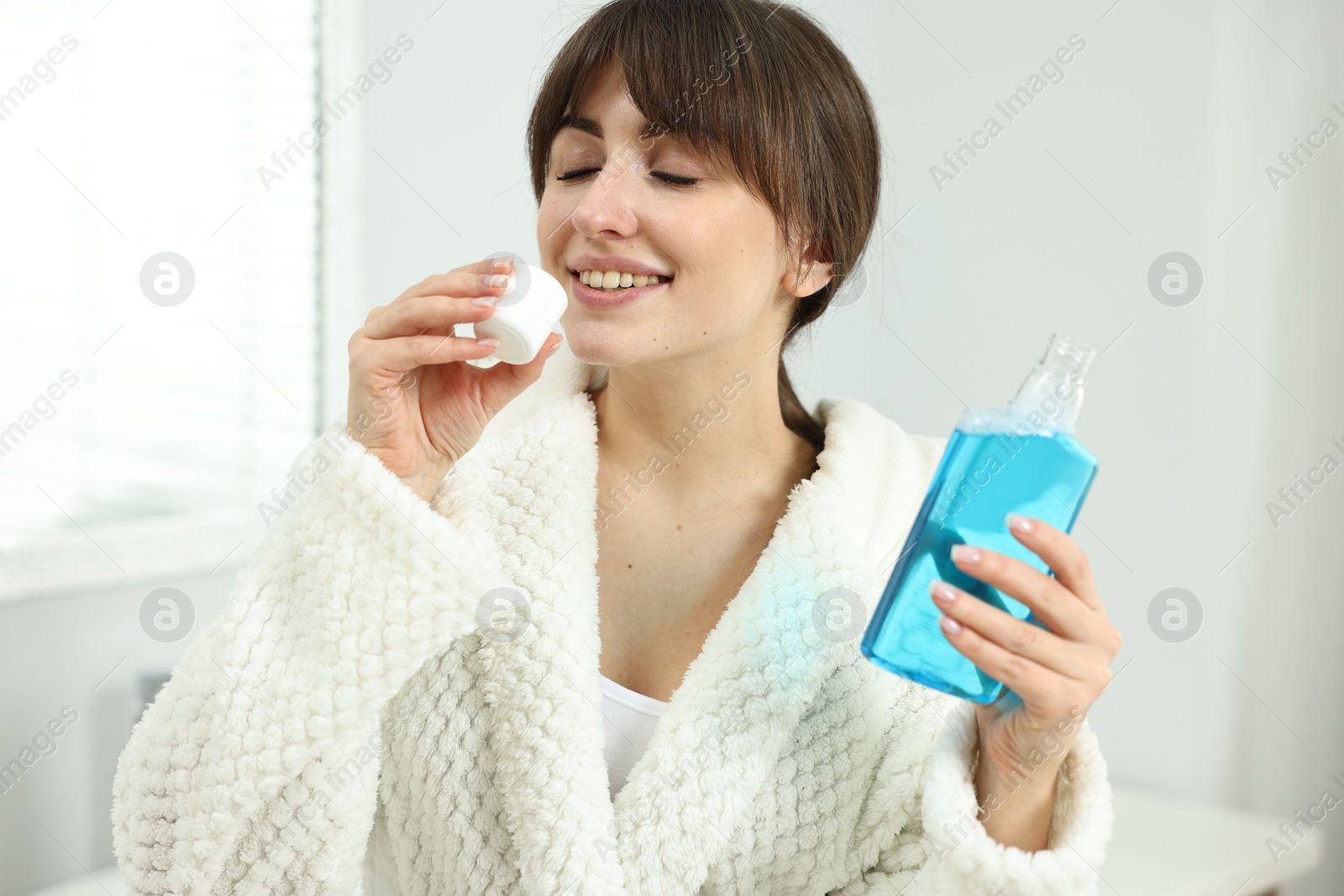 Photo of Young woman using mouthwash in bathroom. Oral hygiene