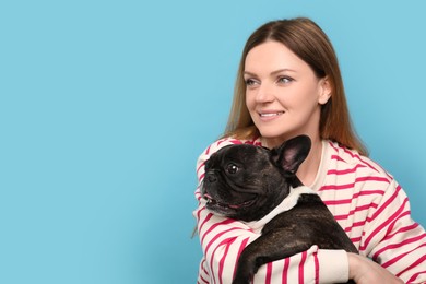 Happy woman hugging cute French Bulldog on light blue background, space for text