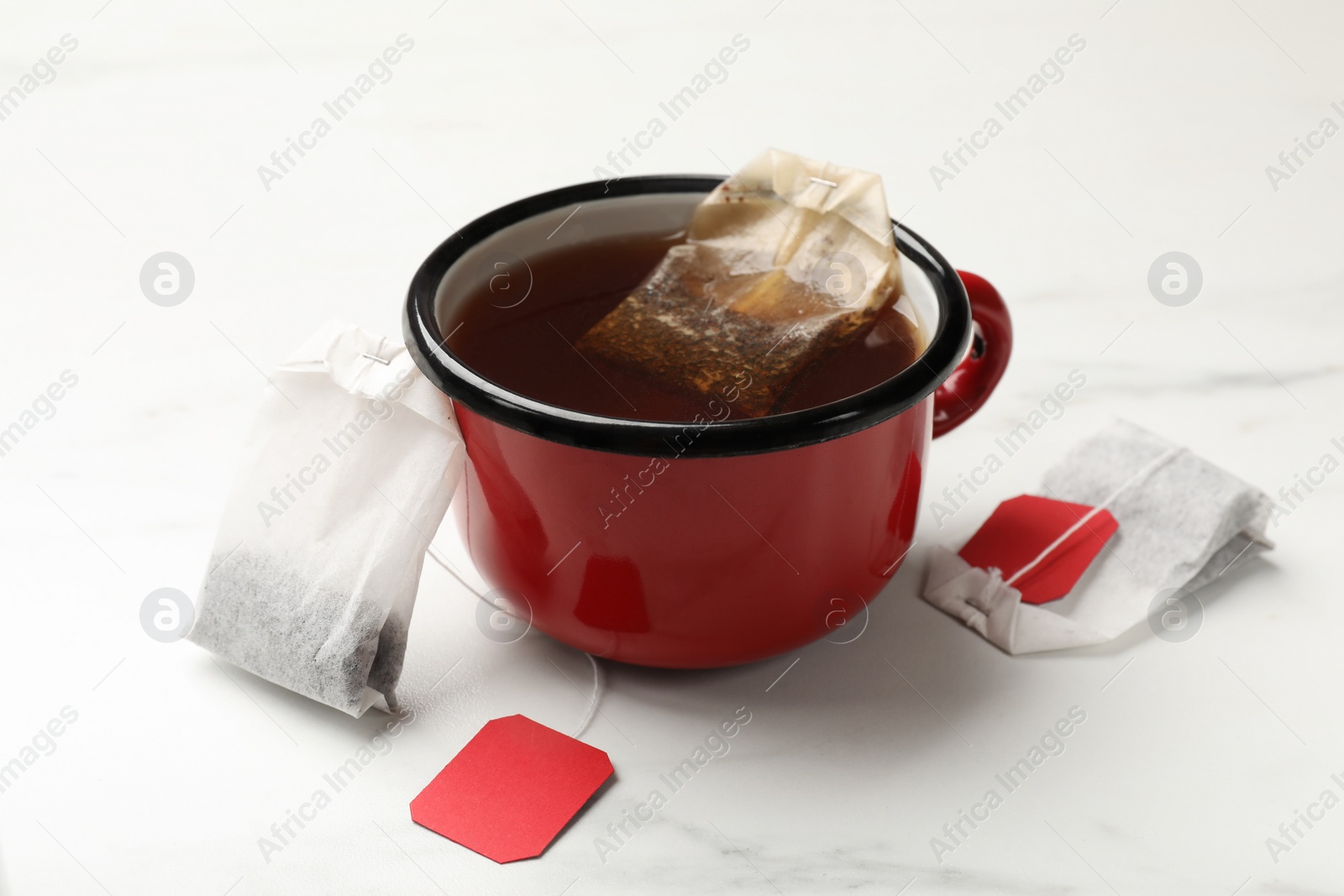 Photo of Tea bags and cup of hot beverage on white table, closeup