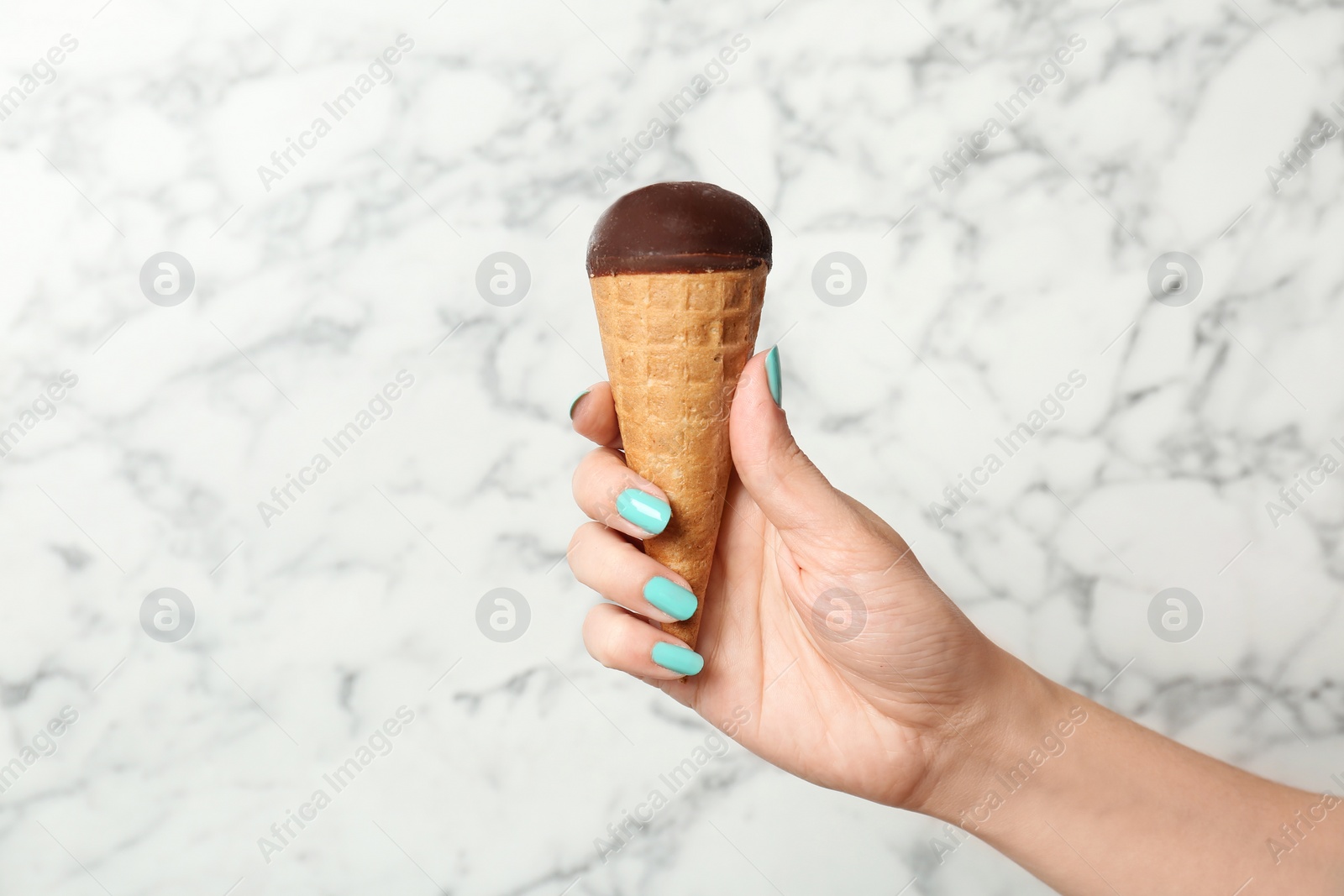 Photo of Woman holding yummy ice cream on marble background. Focus on hand