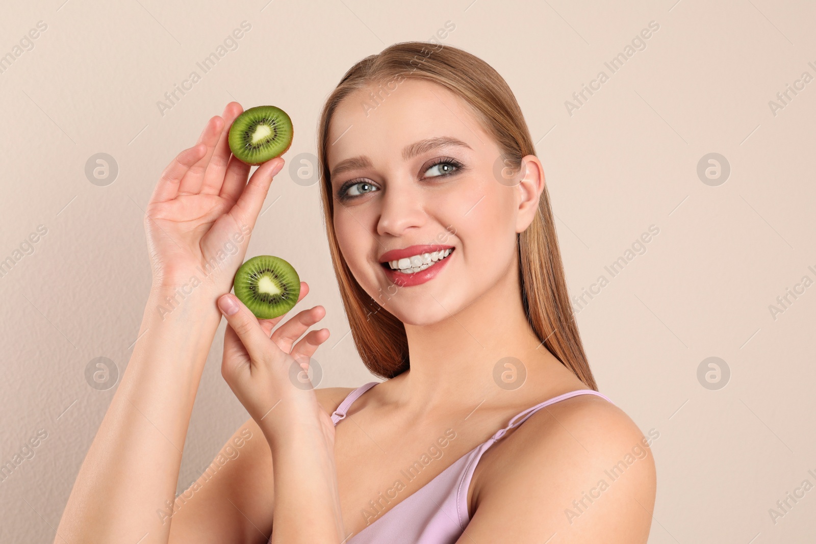 Photo of Young woman with cut kiwi on beige background. Vitamin rich food