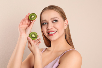 Young woman with cut kiwi on beige background. Vitamin rich food