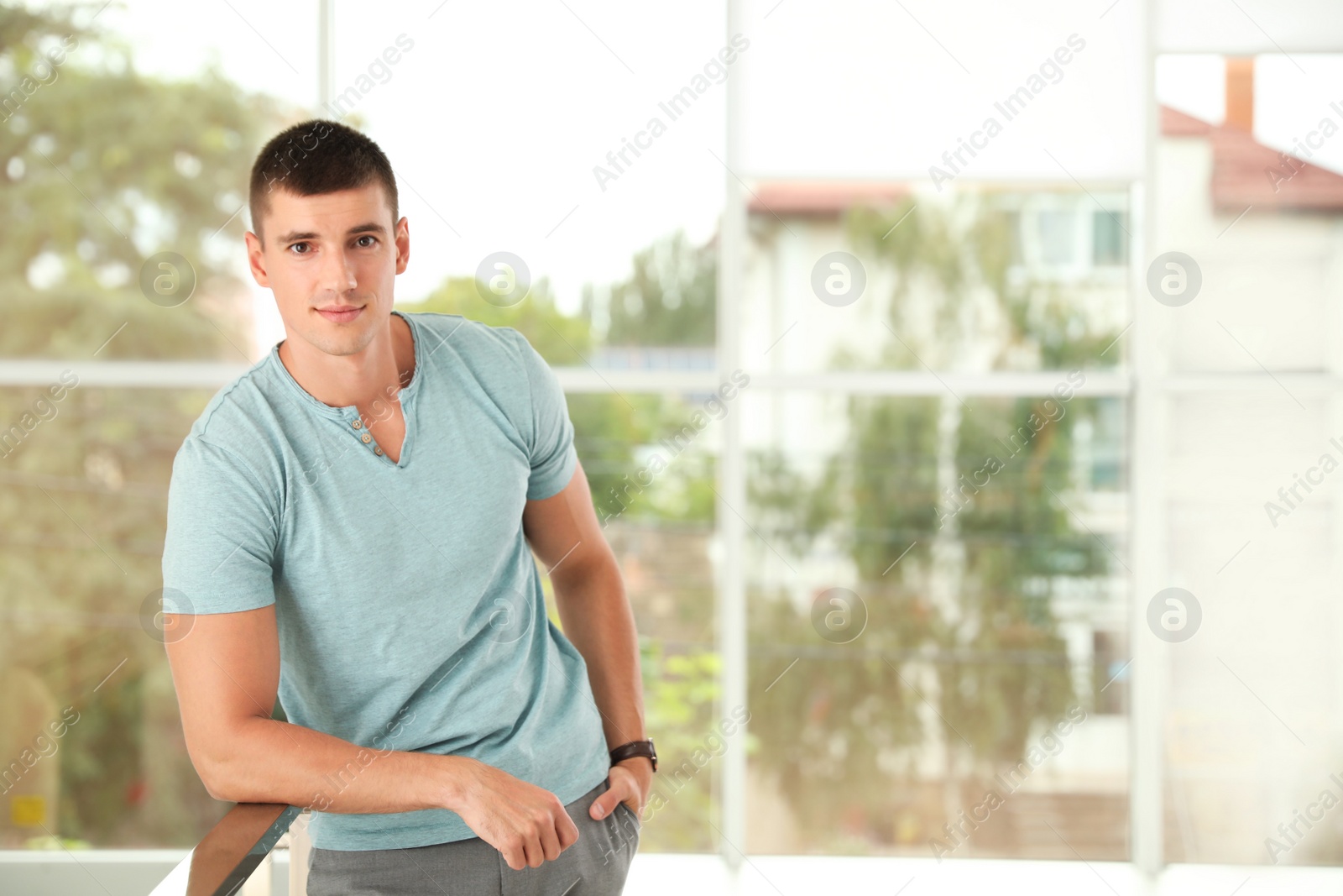 Photo of Portrait of handsome young man leaning on railing indoors. Space for text