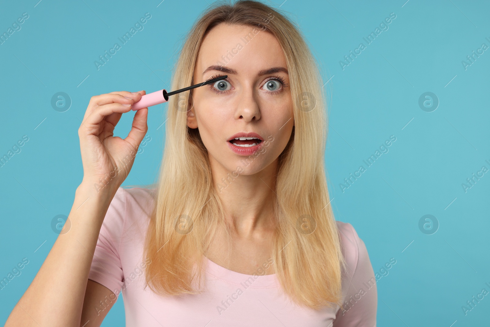 Photo of Beautiful woman applying mascara on light blue background