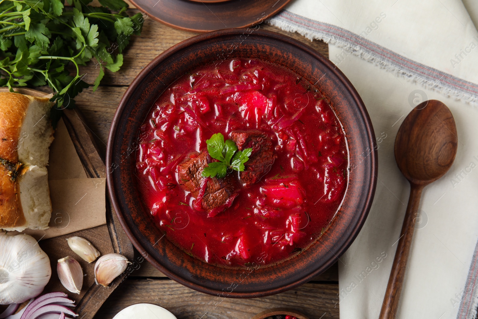 Photo of Stylish brown clay bowl with Ukrainian borsch served on wooden table, flat lay
