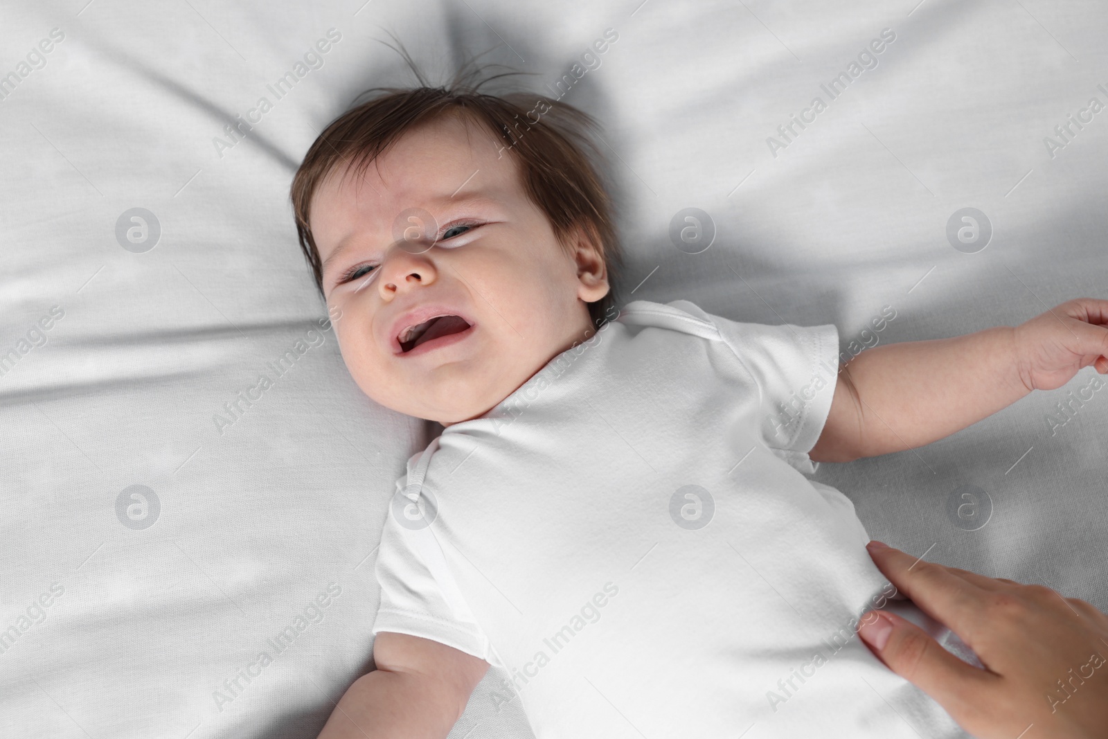 Photo of Cute little baby crying on bed, closeup
