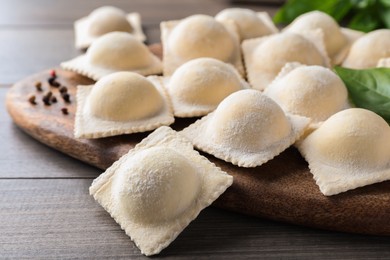 Photo of Uncooked ravioli, basil and peppercorns on wooden table, closeup