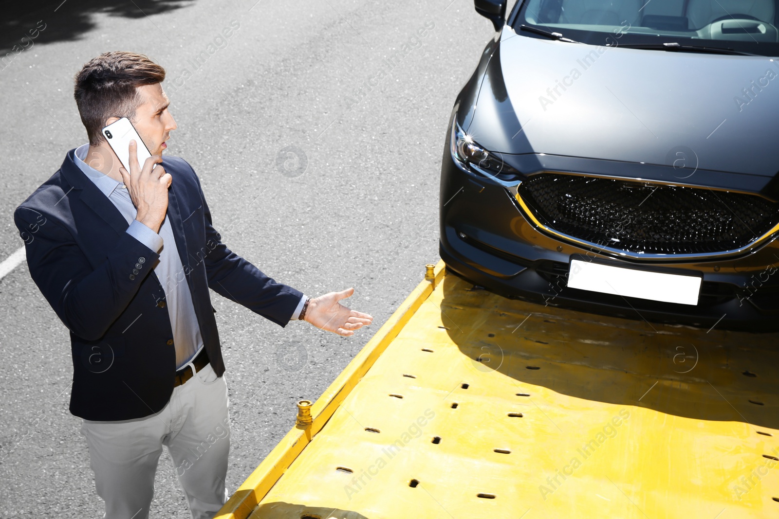 Photo of Man talking on phone near broken car and tow truck outdoors