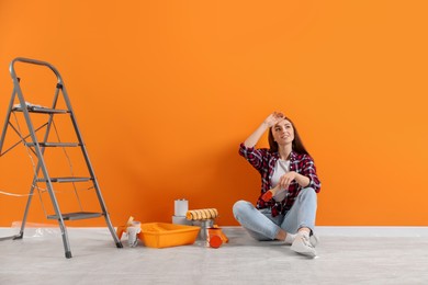 Photo of Designer with brush and painting equipment near freshly painted orange wall indoors