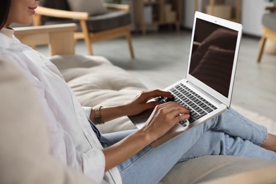 Photo of Young woman working with laptop on sofa at home, closeup