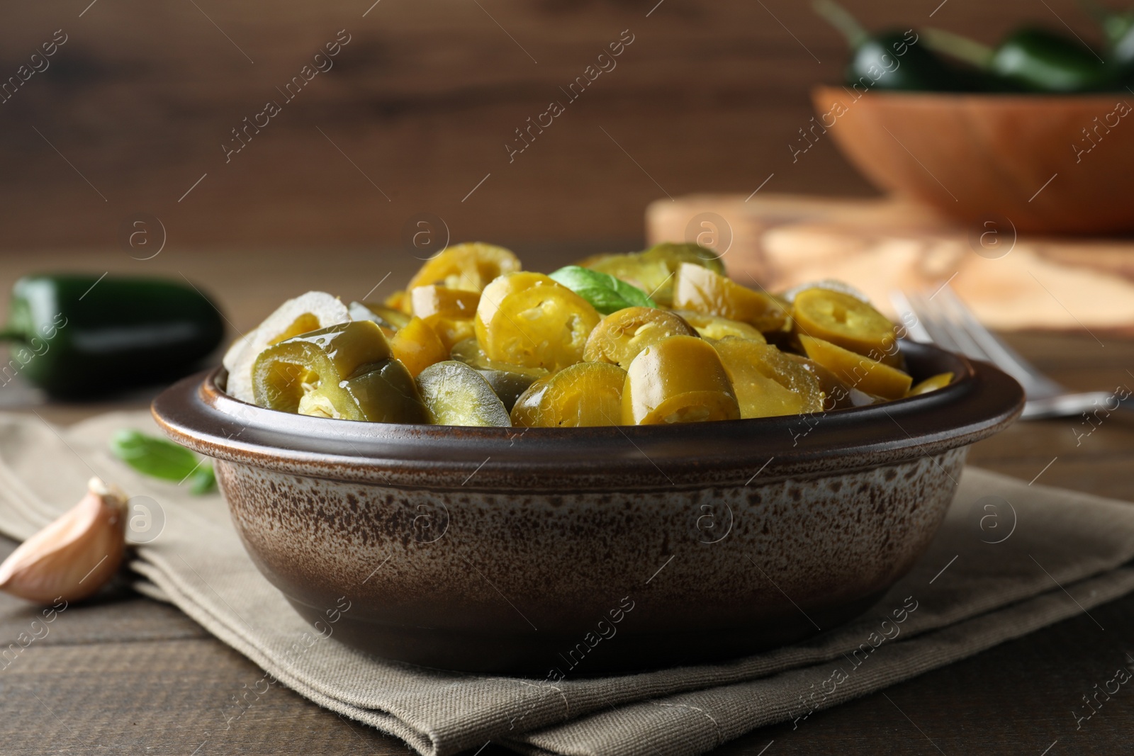 Photo of Bowl with slices of pickled green jalapeno peppers on wooden table