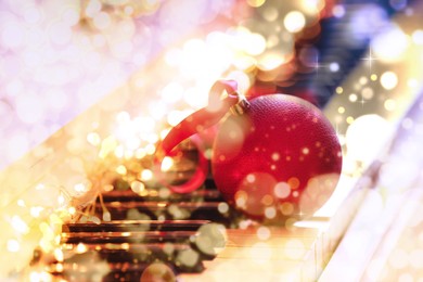 Beautiful red bauble and fairy lights on piano keys, closeup. Christmas music