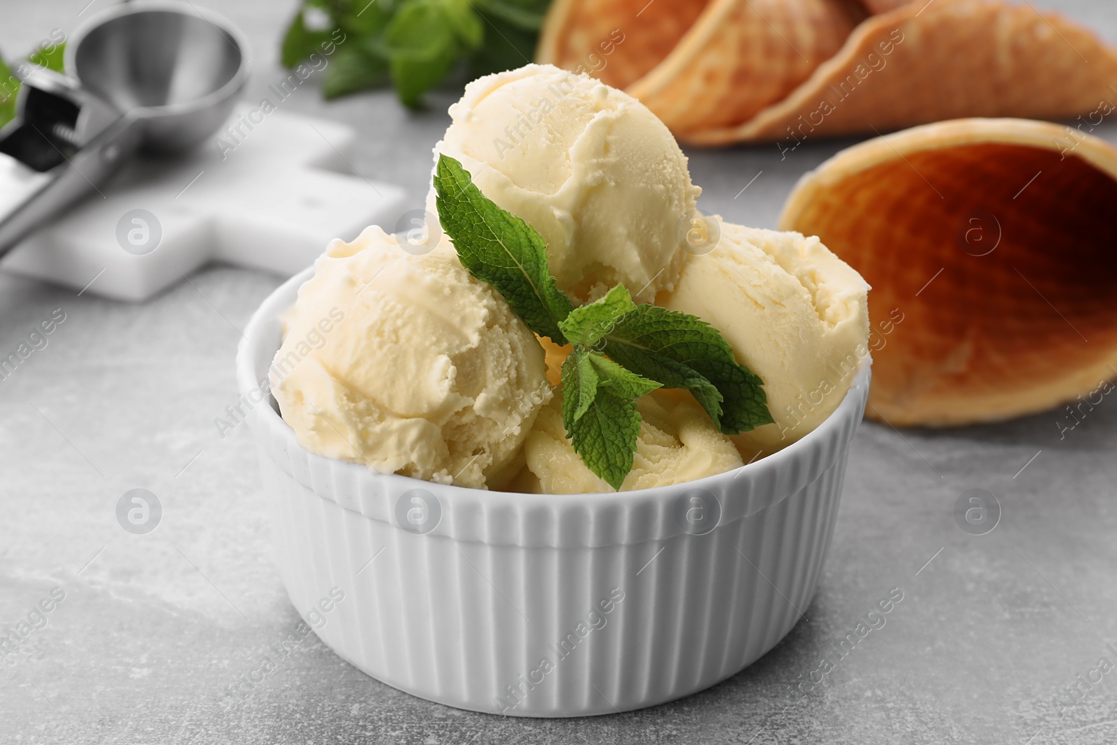 Photo of Delicious vanilla ice cream with mint on light grey table, closeup